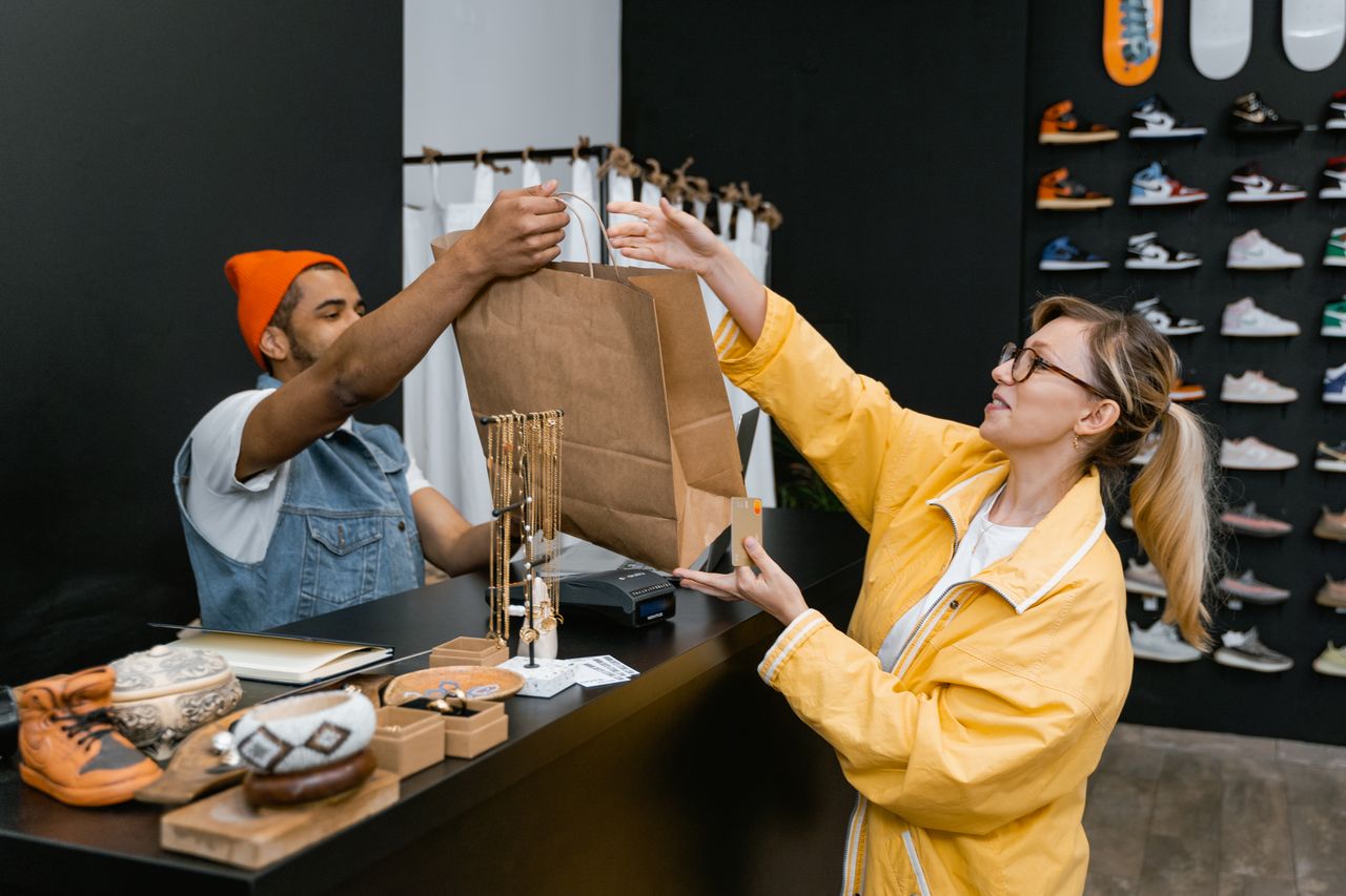 About A customer and cashier exchange items at a fashionable sneaker store counter.
